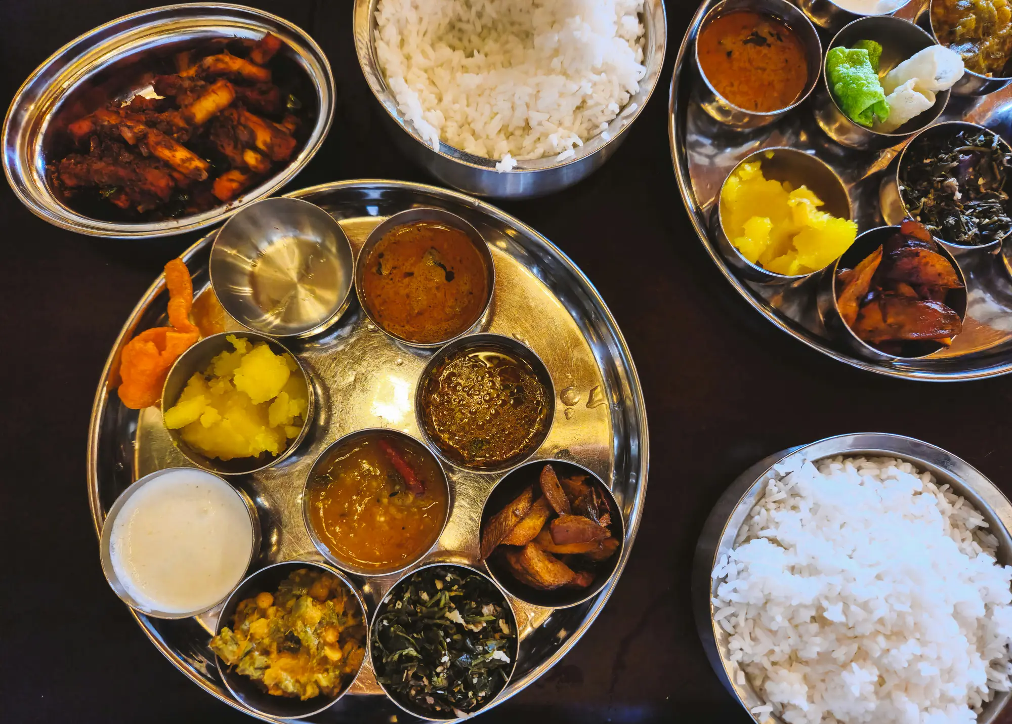 Zwei komplette indische Thalis mit Reis, Dal und mehreren Currys, von oben auf einem dunklen Tisch fotografiert.
