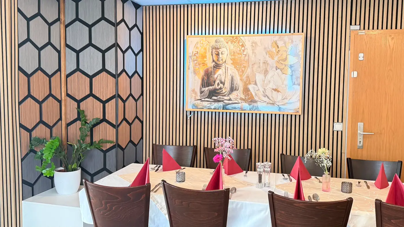 Lange, für eine Gruppe eingedeckte Tafel vor der Lattenwand mit dem goldenen Buddha-Bild; links die Wabenpaneele der Raumecke.