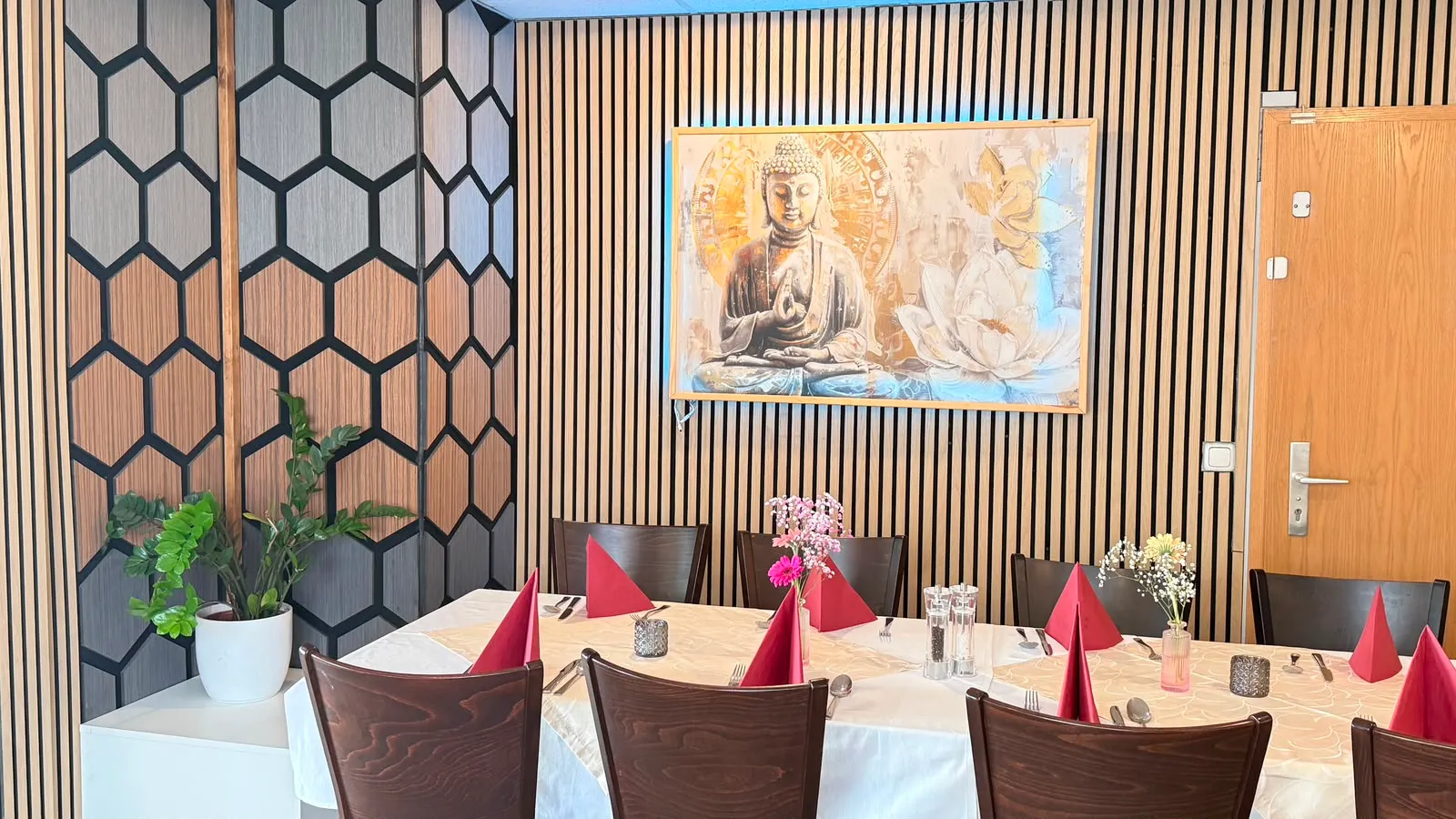 Lange, für eine Gruppe eingedeckte Tafel vor der Lattenwand mit dem goldenen Buddha-Bild; links die Wabenpaneele der Raumecke.