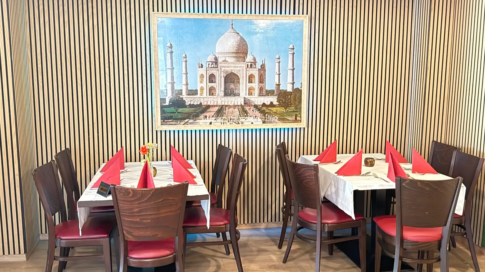 Zwei eingedeckte Tische vor der Lattenwand, darüber das große Taj-Mahal-Bild.