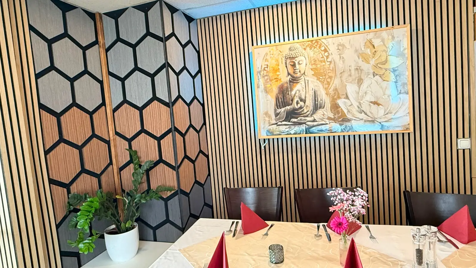 Die Wabenpaneele der Raumecke mit Grünpflanze, rechts das Buddha-Bild über der eingedeckten Tafel.